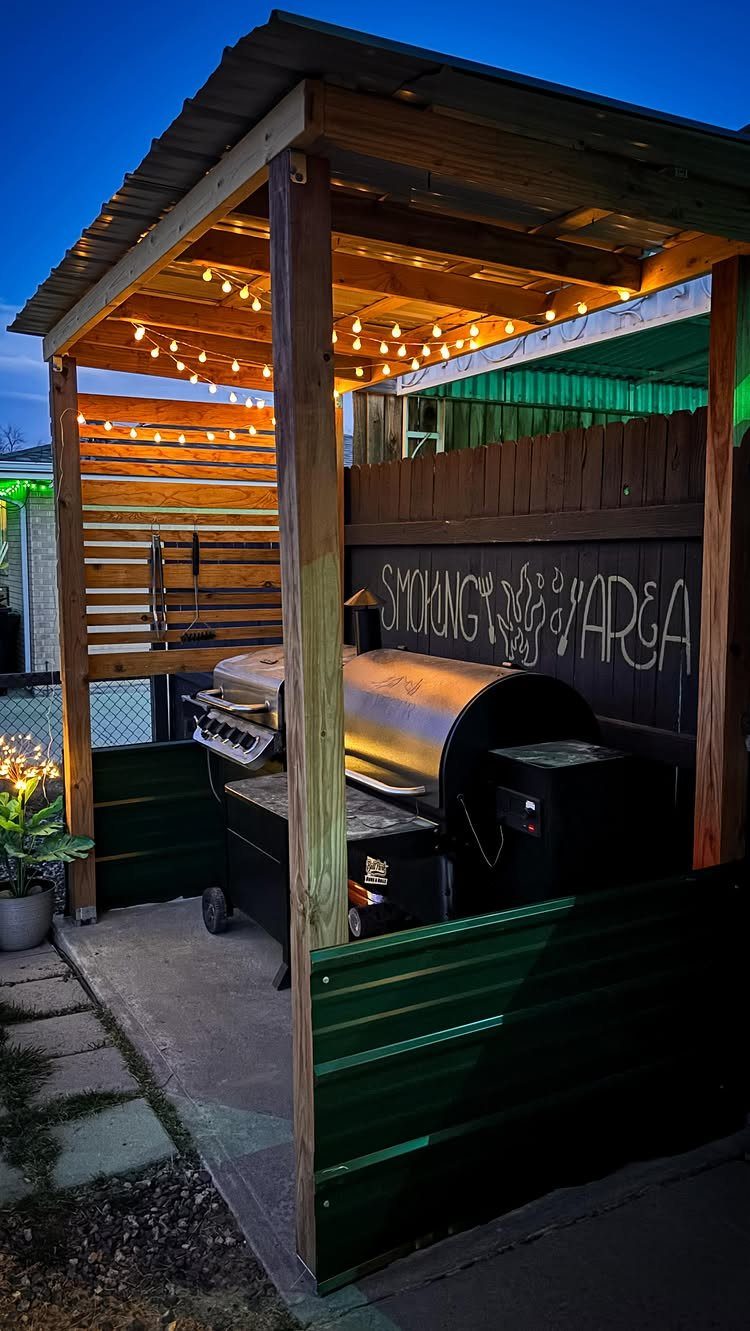 A wooden backyard smoking area shelter with string lights and a black smoker grill inside.