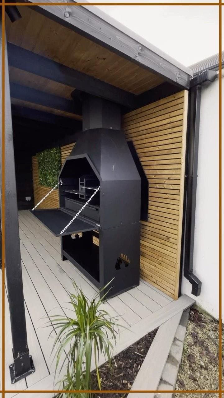 A black metal outdoor barbecue grill situated under a dark wooden ceiling structure on a deck.