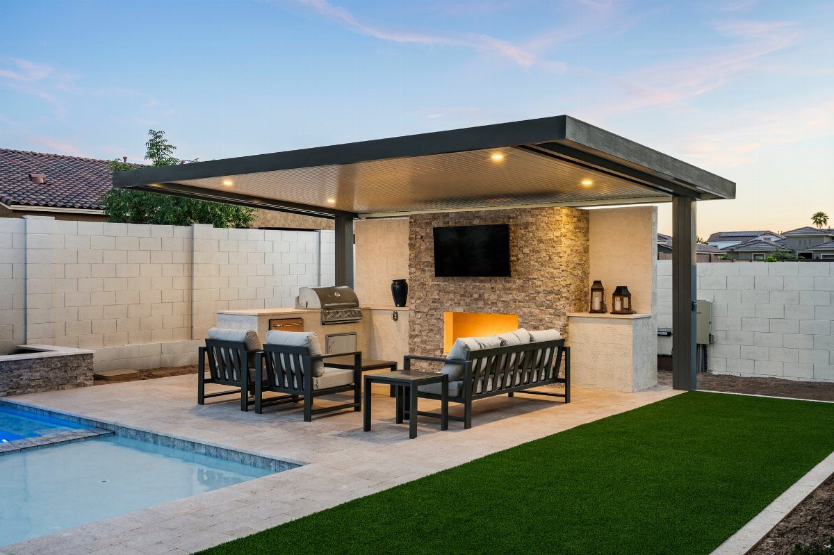 Modern outdoor kitchen and lounge area under a dark flat-roofed pergola next to a pool.