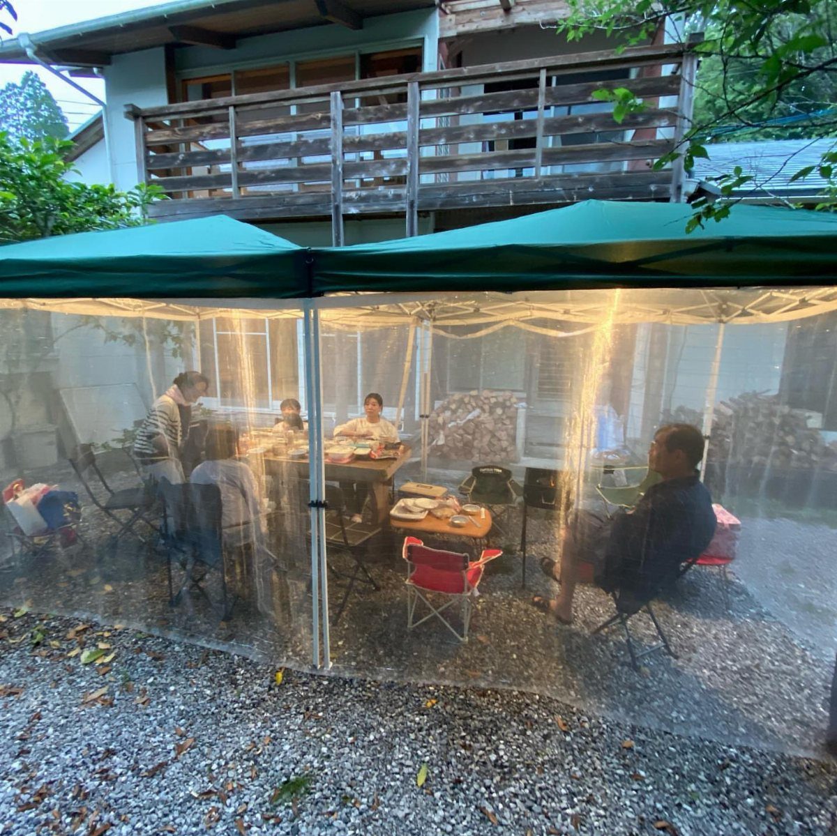 People sitting at a table under a green pop-up canopy with clear plastic walls.