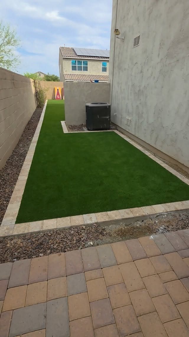 A long, narrow strip of green artificial grass installed in a backyard next to a wall.