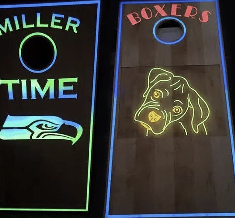 Two wooden cornhole boards with glowing neon-style outlines and colorful designs against a dark background.