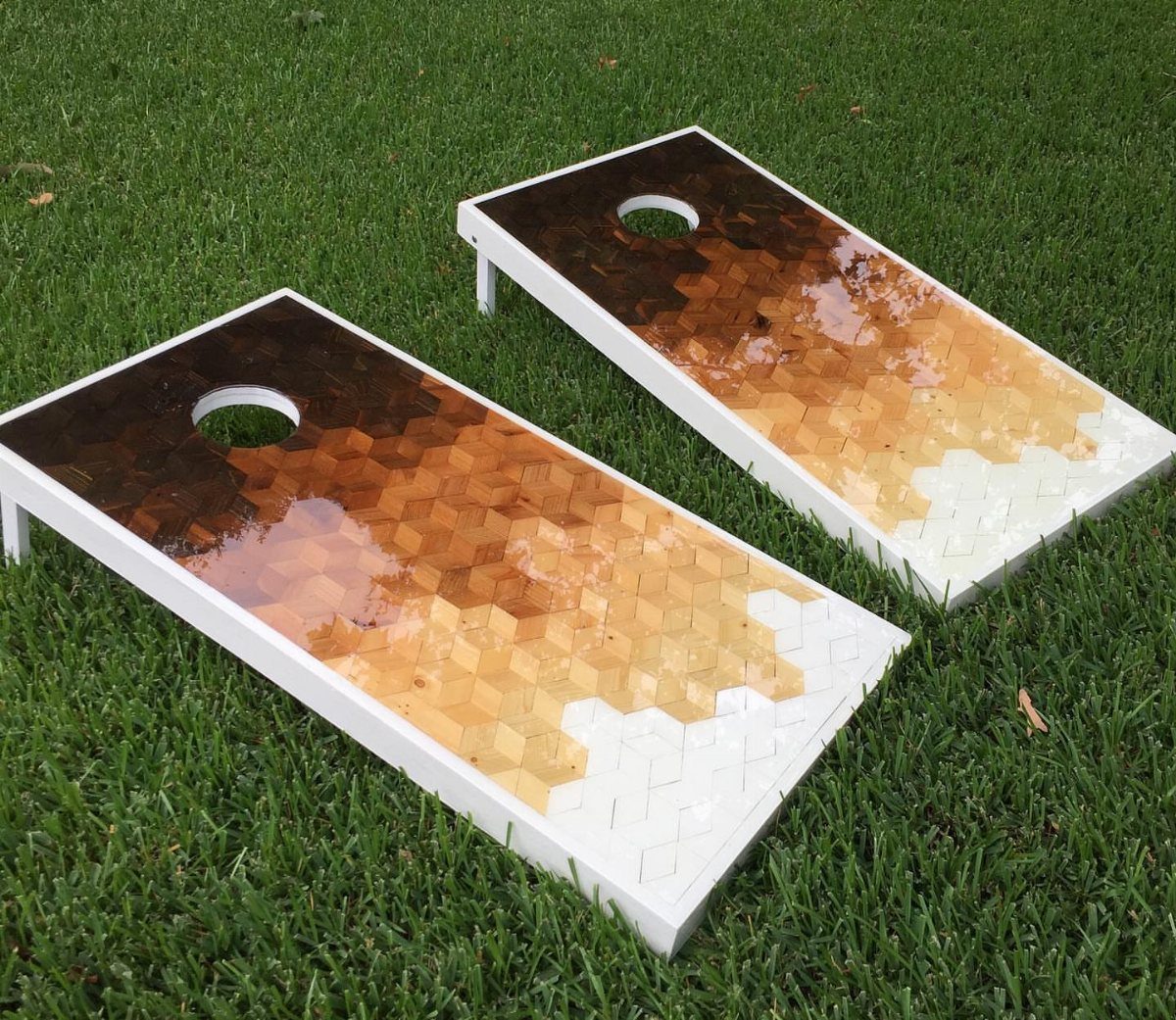 Two cornhole boards with brown and tan hexagonal mosaic patterns resting on green grass.