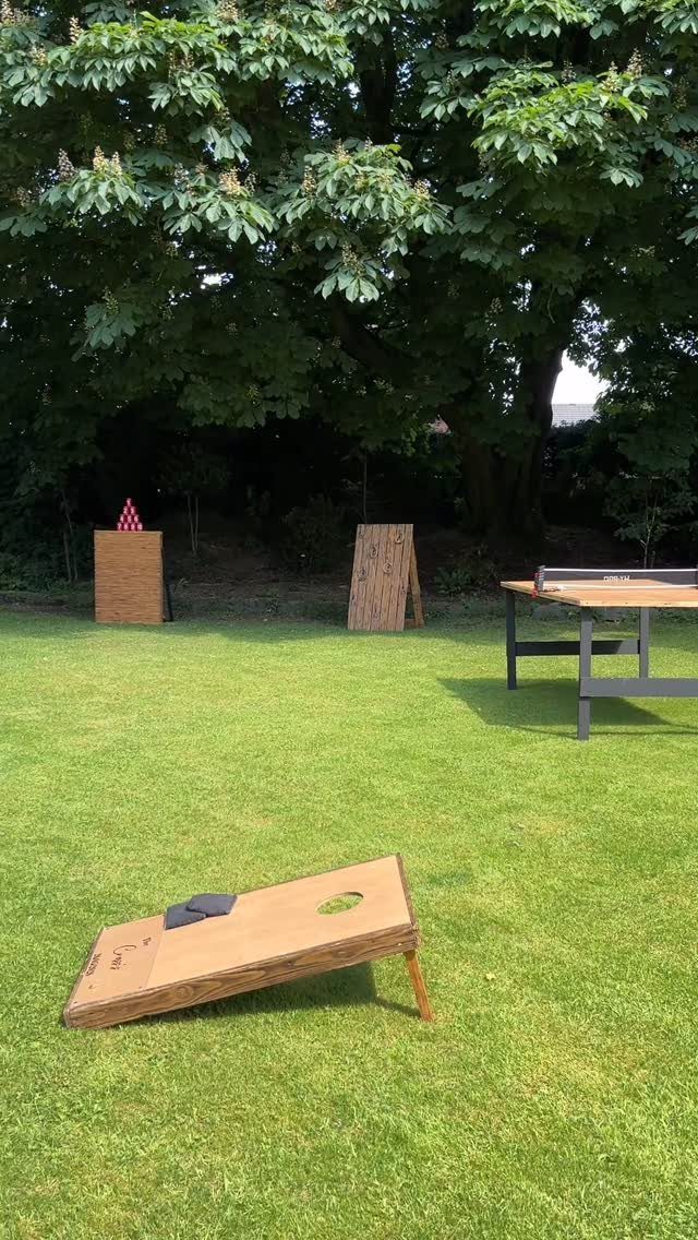A wooden cornhole board resting on a lush green grass lawn in a backyard.