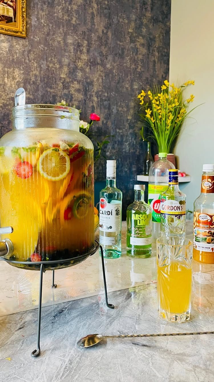 A large glass beverage dispenser filled with fruit-infused yellow liquid on a marble counter.