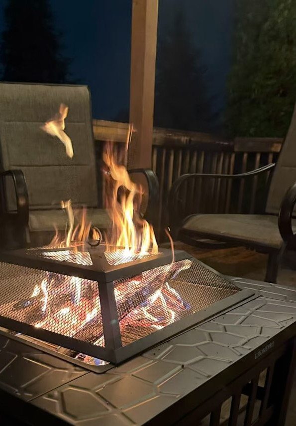 Flames burning inside a metal fire pit on an outdoor patio table at night.