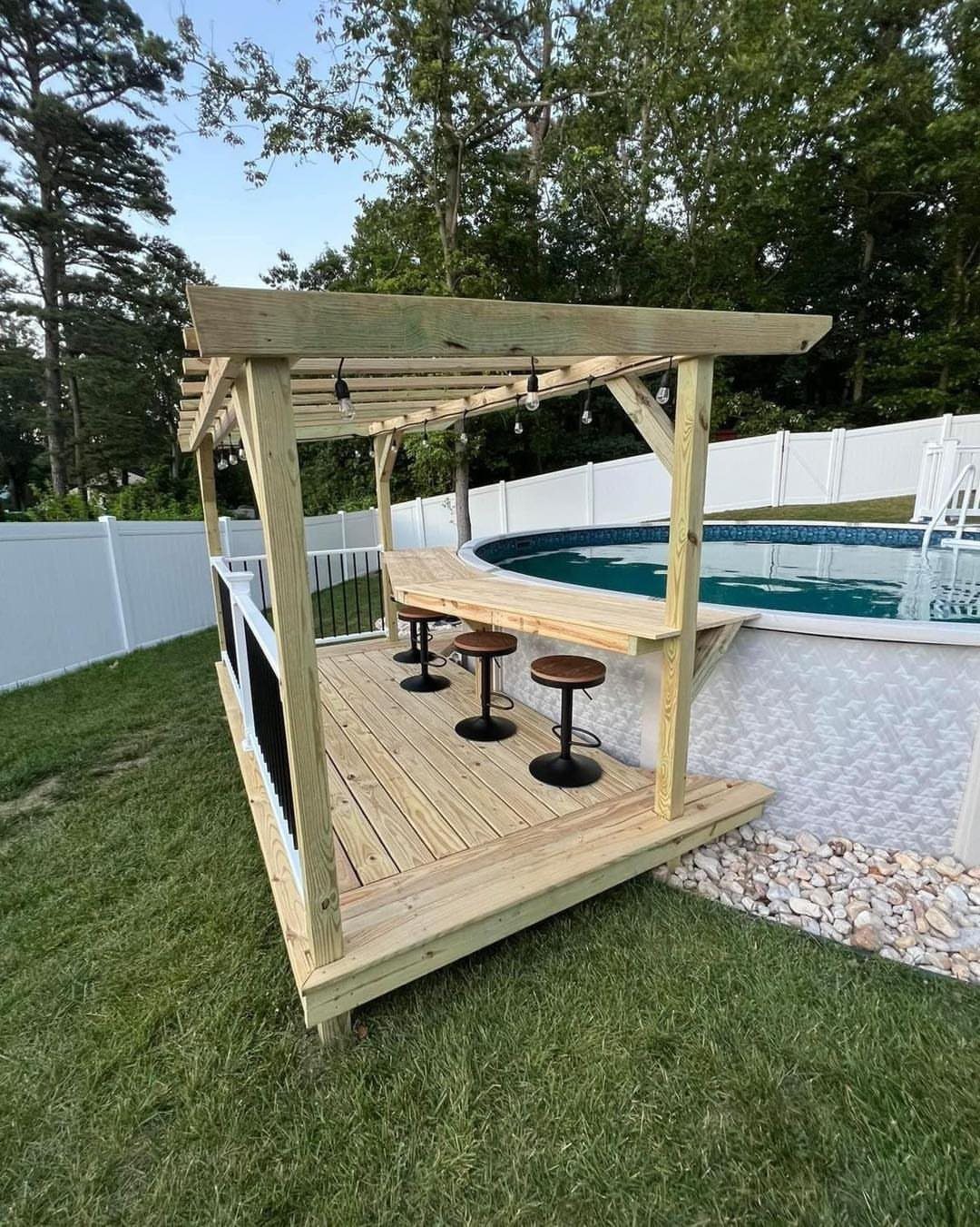 A small wooden deck bar with a pergola roof and stools next to a swimming pool.