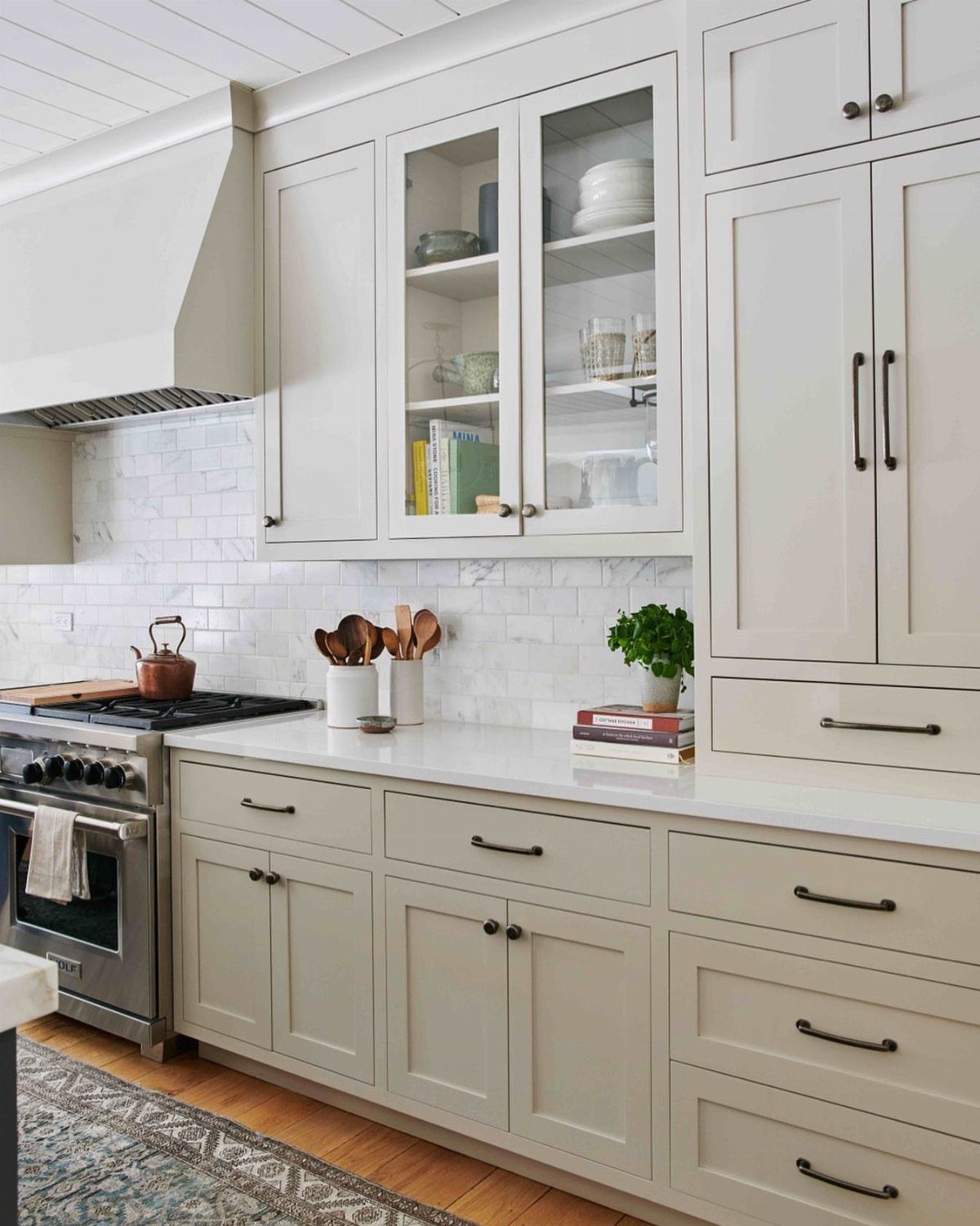 Beige shaker kitchen cabinets with dark hardware and a white marble tile backsplash.