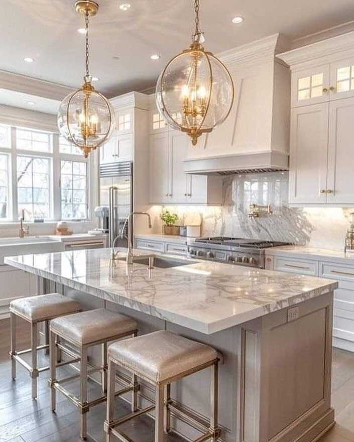 Beige kitchen cabinets paired with a white marble countertop and gold pendant lights.