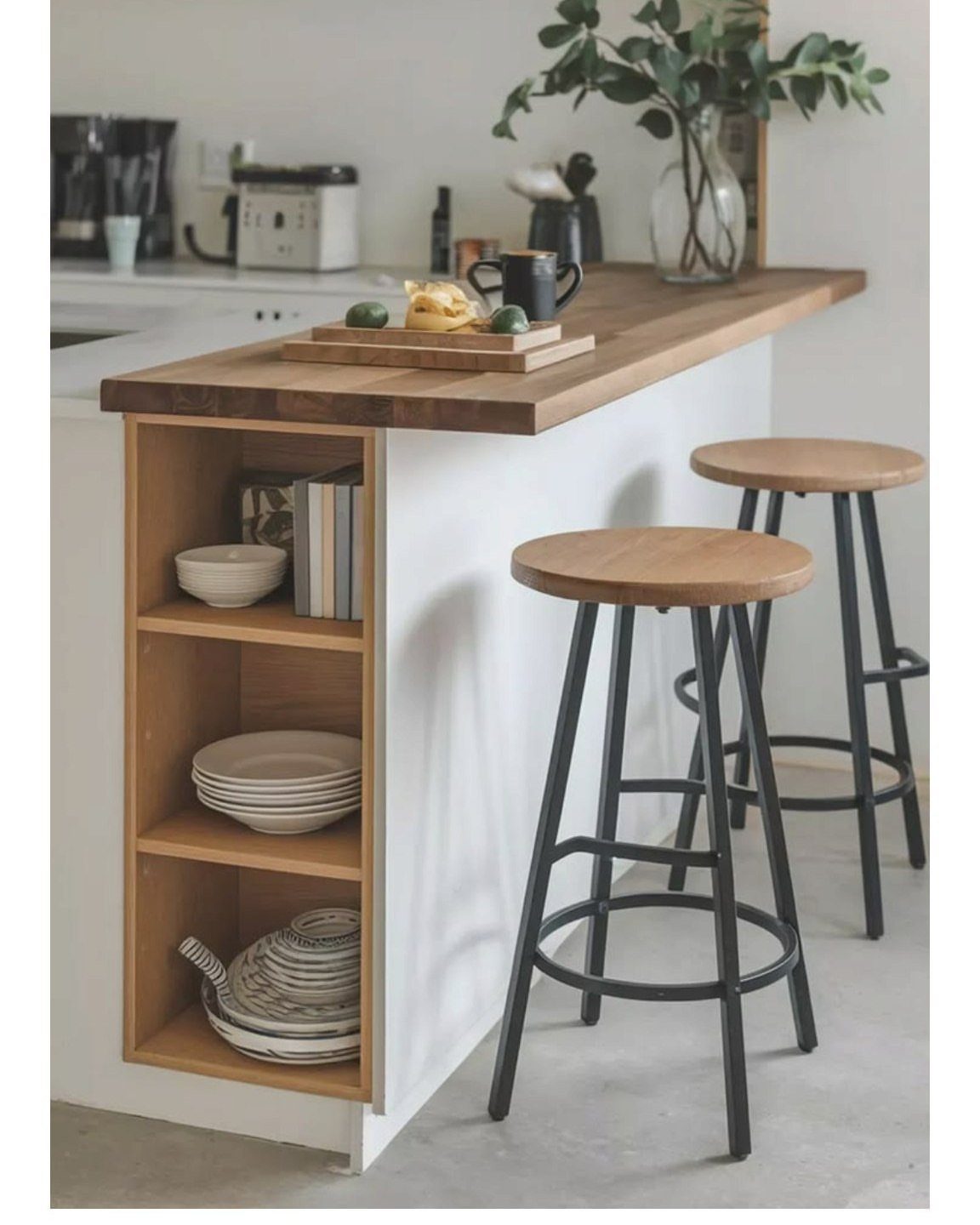 Wooden kitchen island with built-in open shelving and two bar stools on a light floor.
