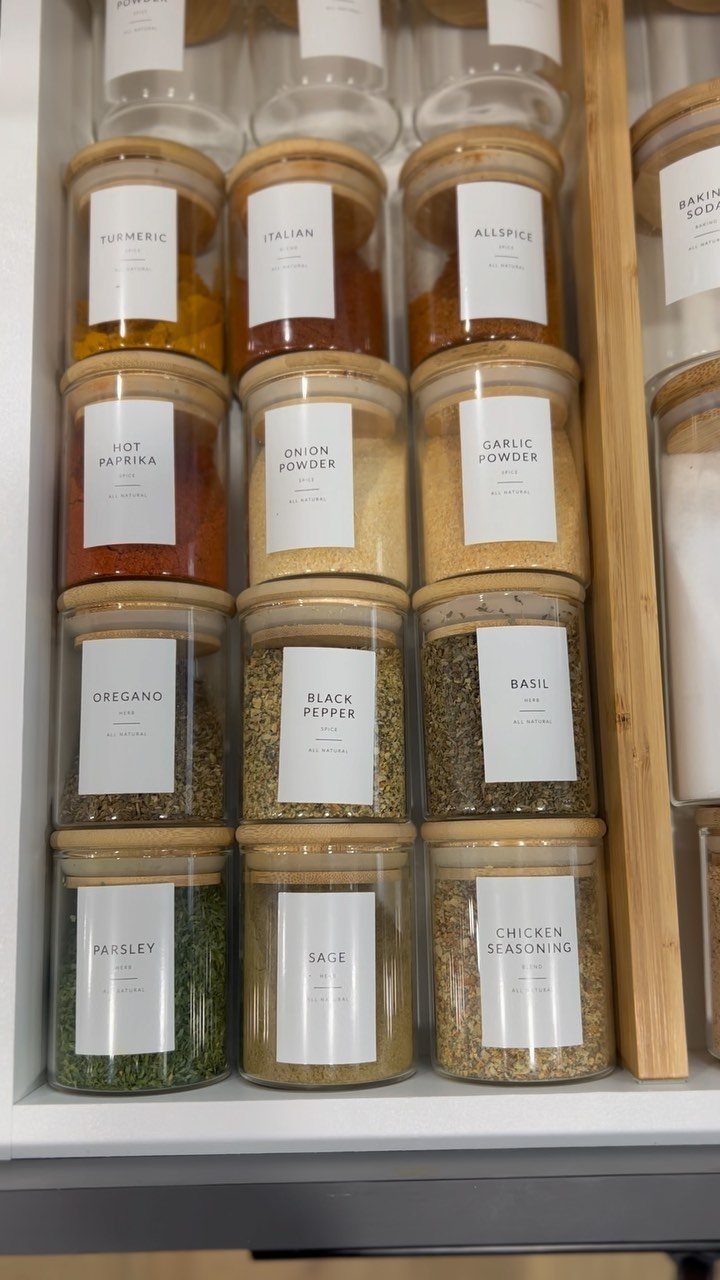 Glass spice jars with wooden lids organized inside a kitchen drawer with dividers.
