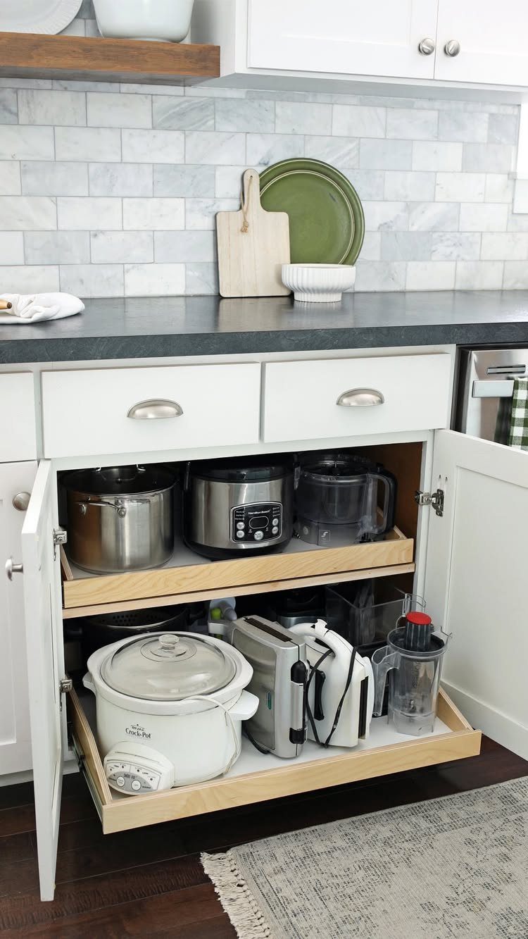 Wooden pull-out drawers inside white kitchen cabinets holding various small kitchen appliances.