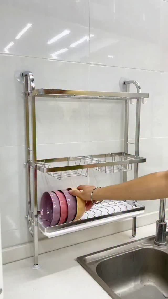 A person placing pink bowls onto a silver metal dish rack mounted above a sink.