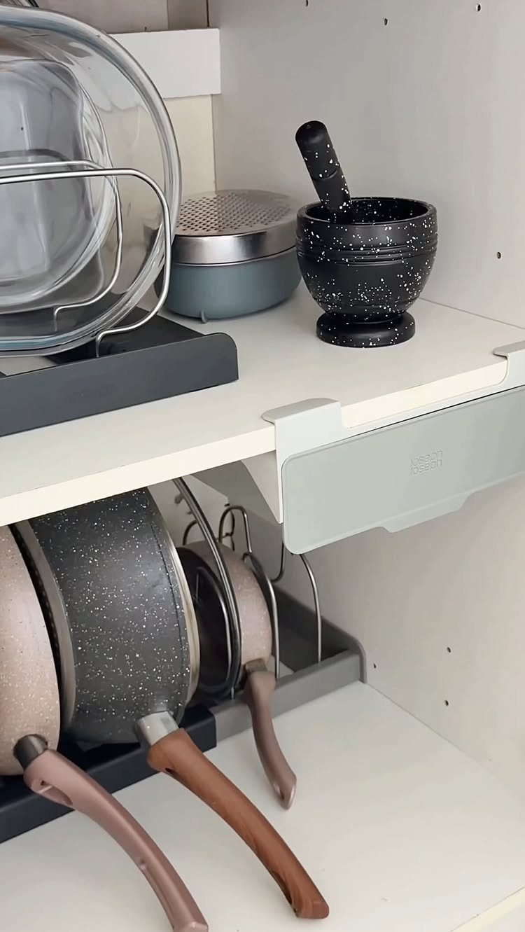 Kitchen cabinet shelves organized with a mortar and pestle, plates, and a pan organizer holding frying pans.