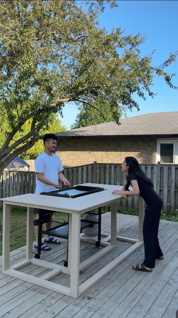 A man and woman standing by a custom outdoor table with a built-in griddle on a wooden deck.