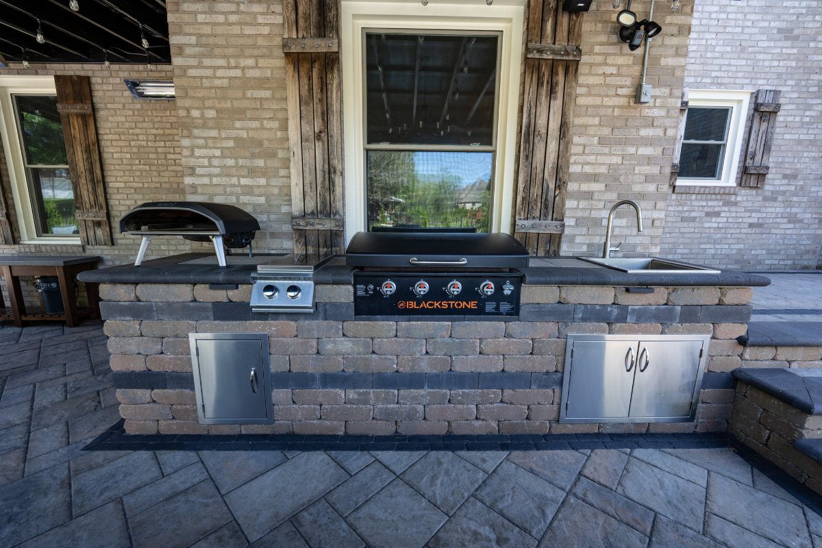 A built-in outdoor kitchen island with a Blackstone griddle, sink, and stainless steel storage cabinets.