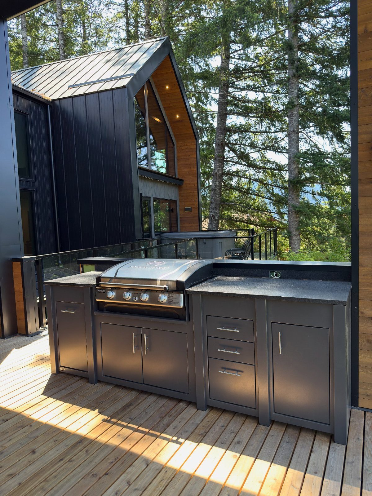 A black outdoor griddle built into dark grey cabinetry on a wooden deck near a modern house.