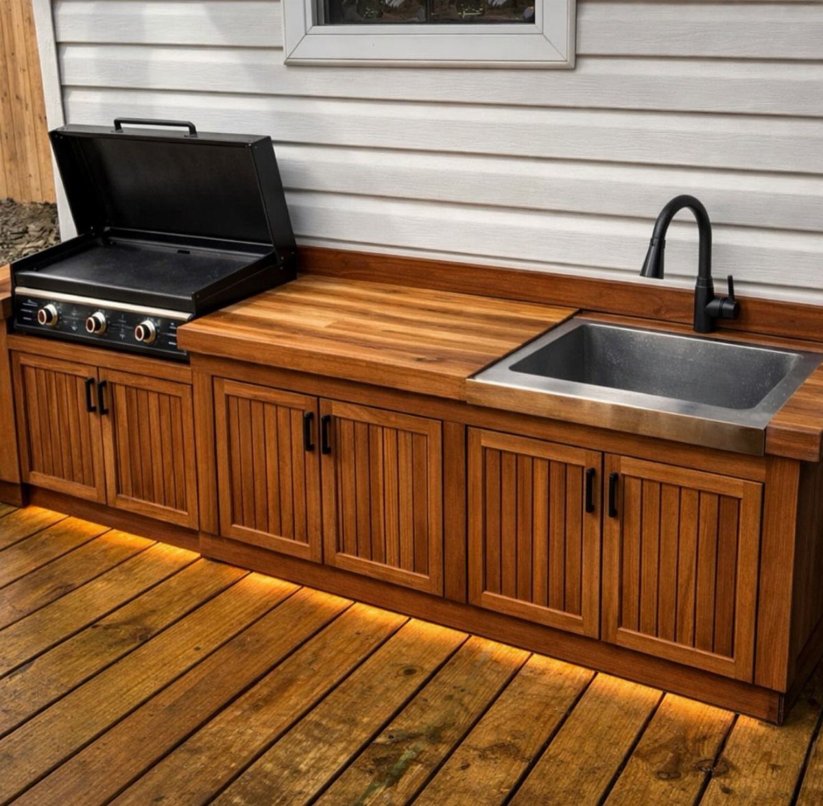 Wooden outdoor kitchen island with a built-in griddle and a stainless steel sink on a deck.