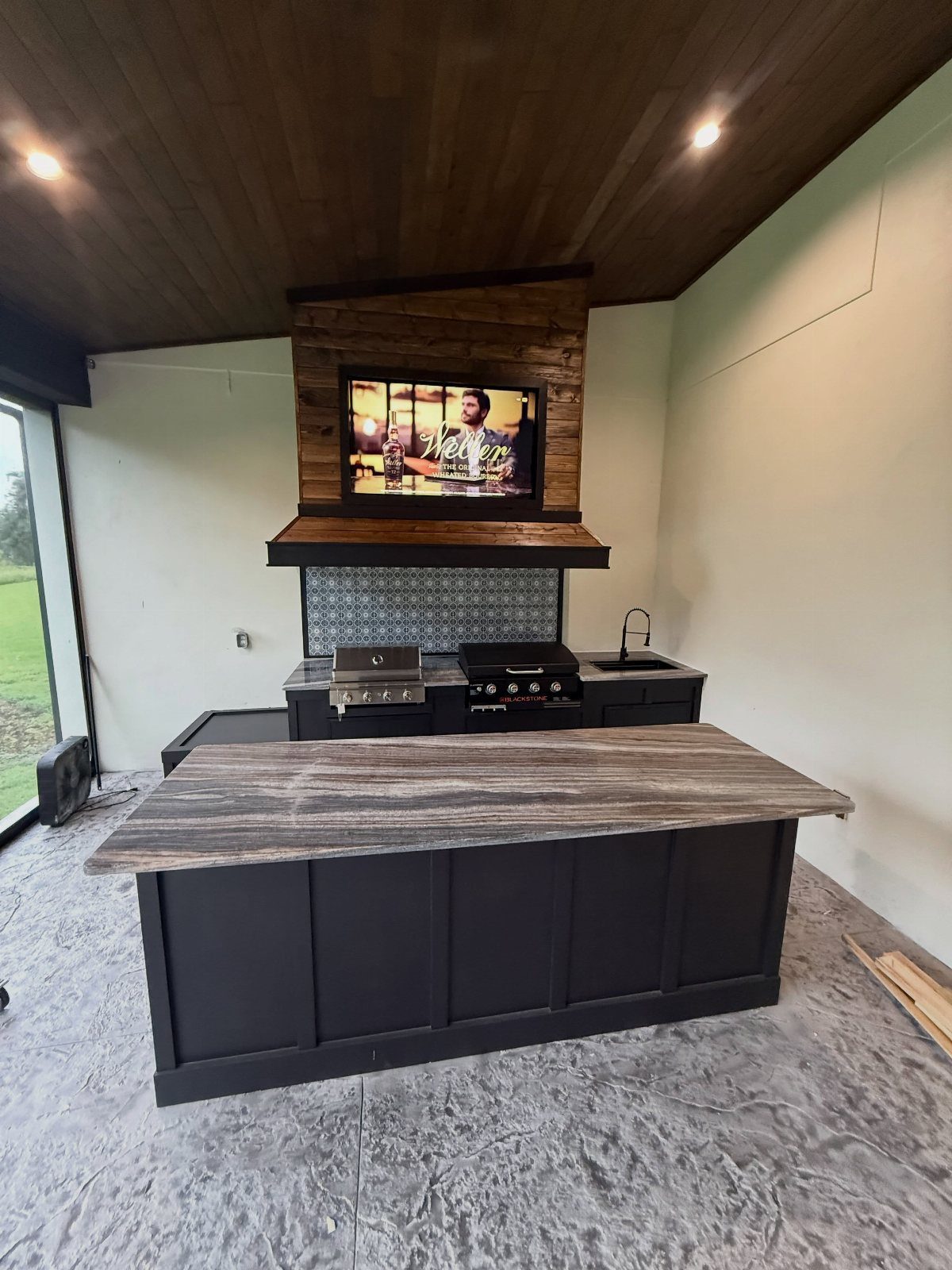 Black outdoor kitchen island with stone countertop in a modern patio setting.