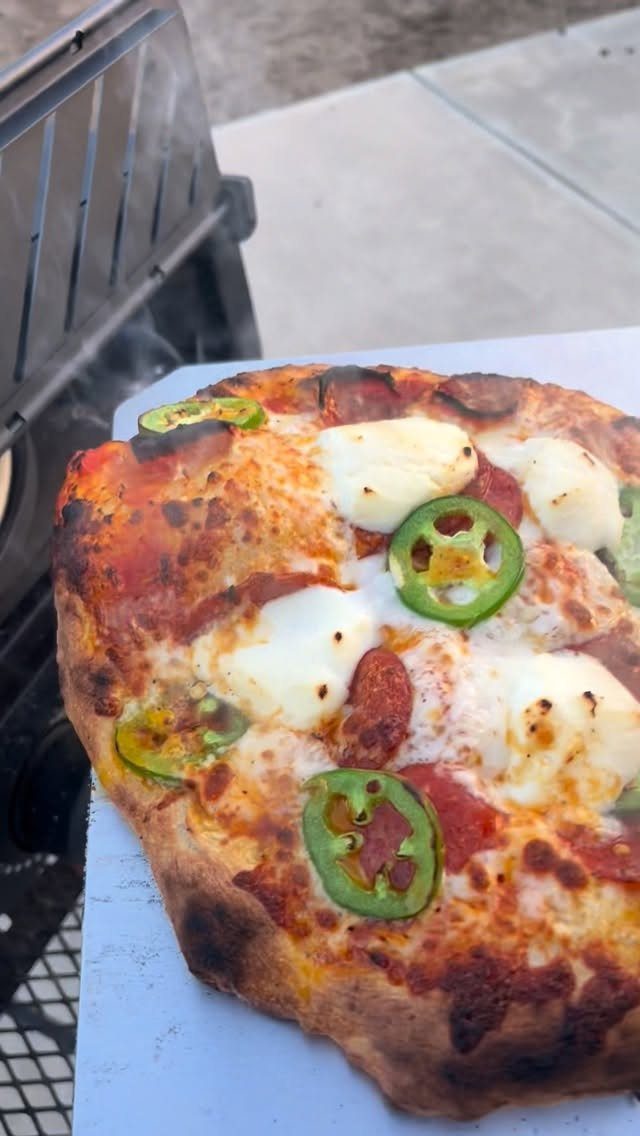 A freshly baked pizza topped with mozzarella, pepperoni, and jalapeño slices on a white surface.