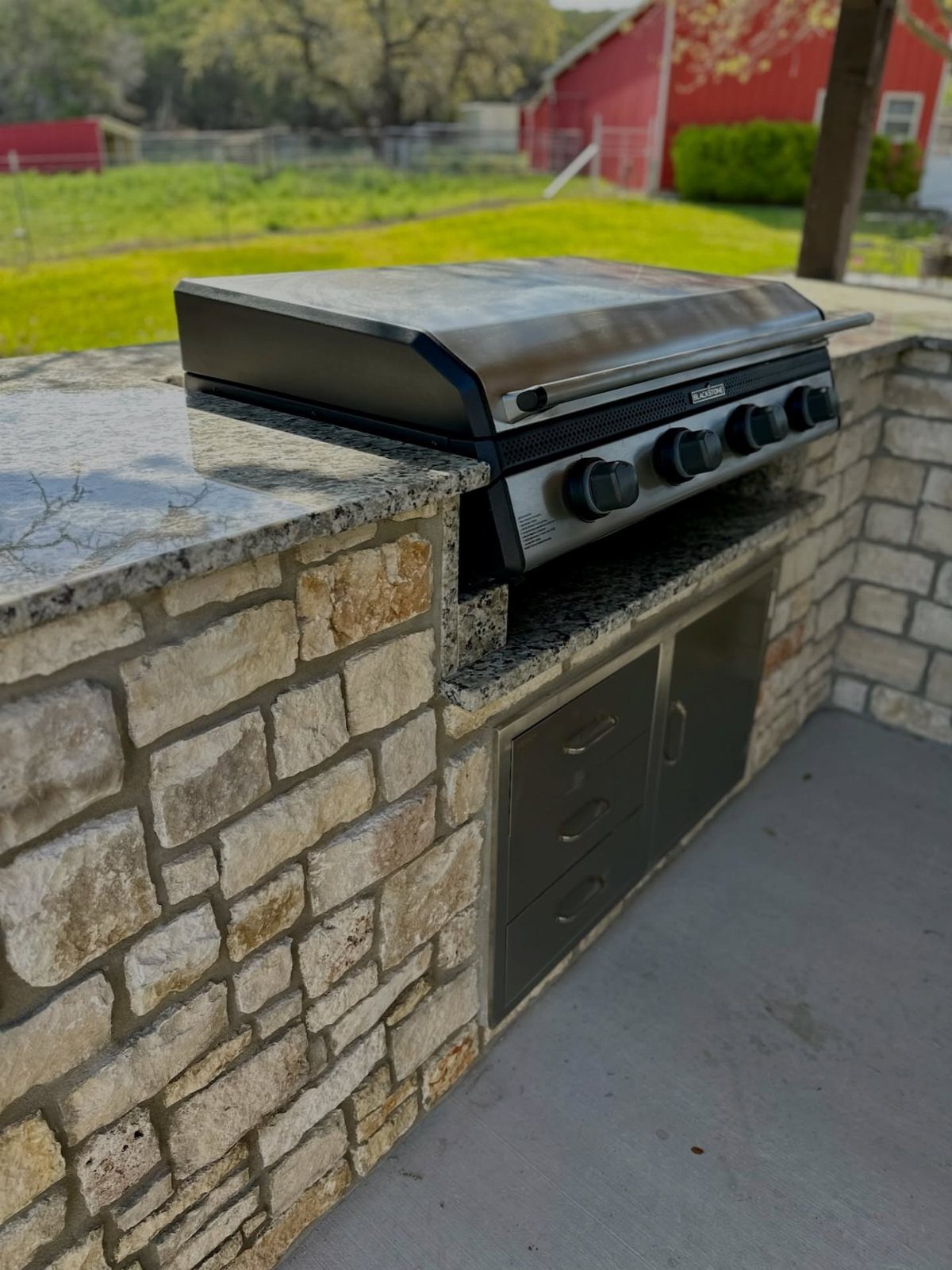A black Blackstone griddle built into a stone outdoor kitchen island with granite countertops.