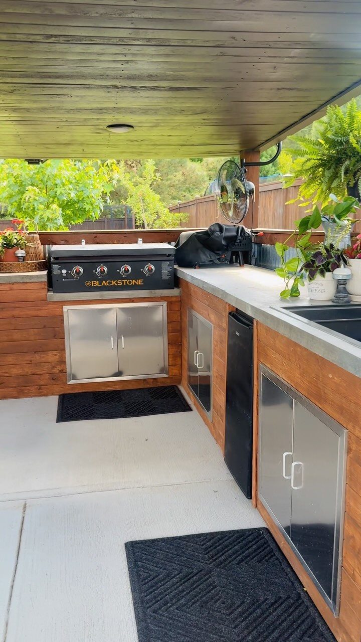 Blackstone griddle built into a wooden outdoor kitchen island with concrete countertops and stainless steel cabinets.