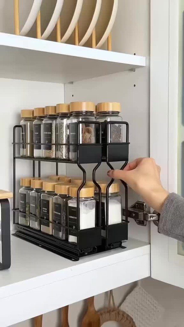A hand reaches into a white cabinet to grab a spice jar from a black metal rack.