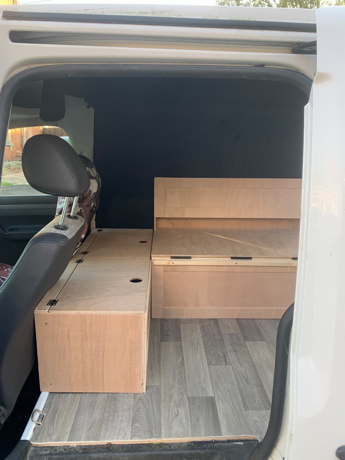 Custom wooden storage boxes installed inside a camper van with grey wood flooring.