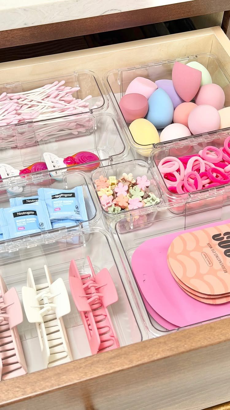 Clear acrylic drawer dividers organizing colorful hair accessories and makeup sponges in a wooden drawer.