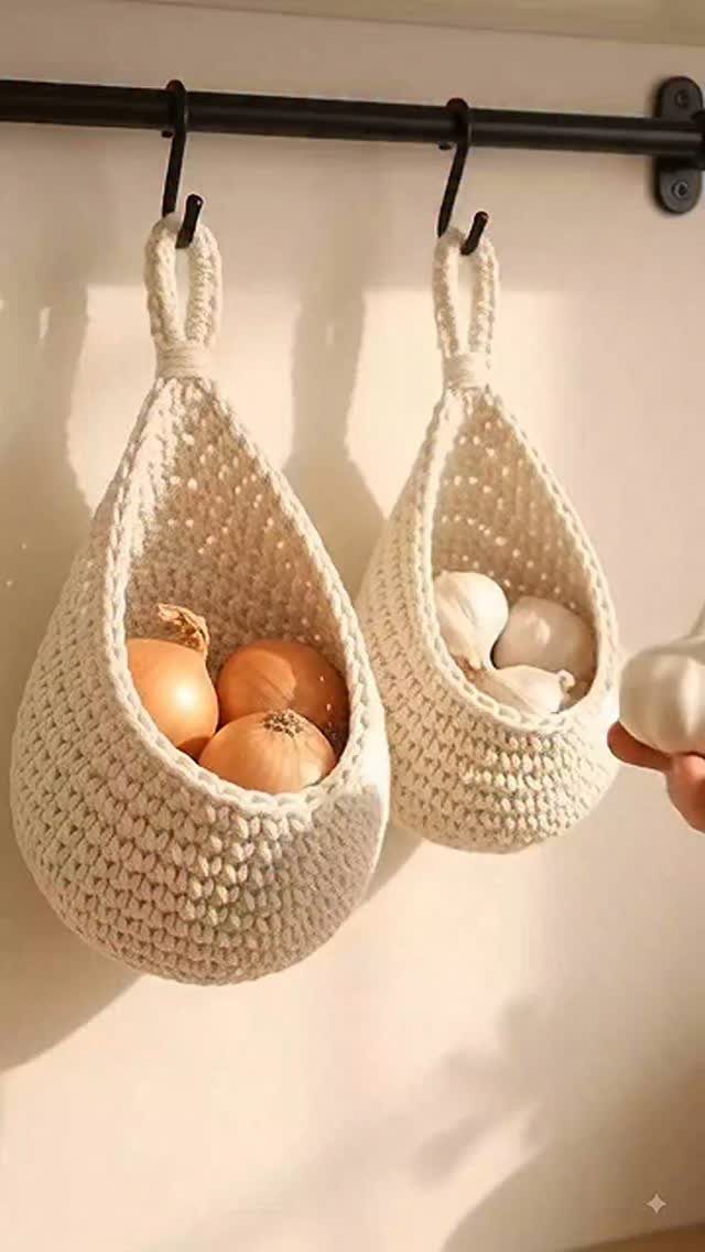 Two white crocheted hanging baskets containing onions and garlic suspended from a black rod.