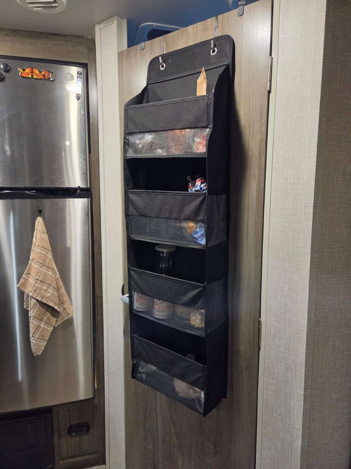 Black fabric over-the-door organizer hanging on a wooden door filled with snacks.