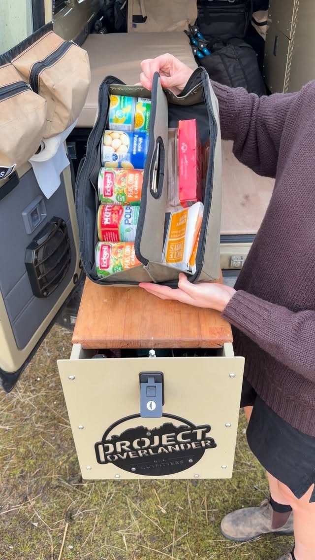 A person holding an organized storage bag filled with canned food items over a vehicle drawer.
