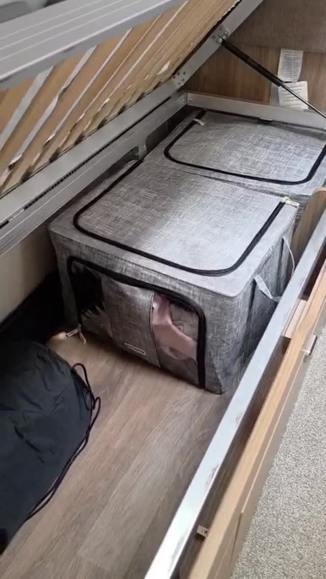Two grey fabric storage bins tucked under a slatted wooden bed frame in a camper.
