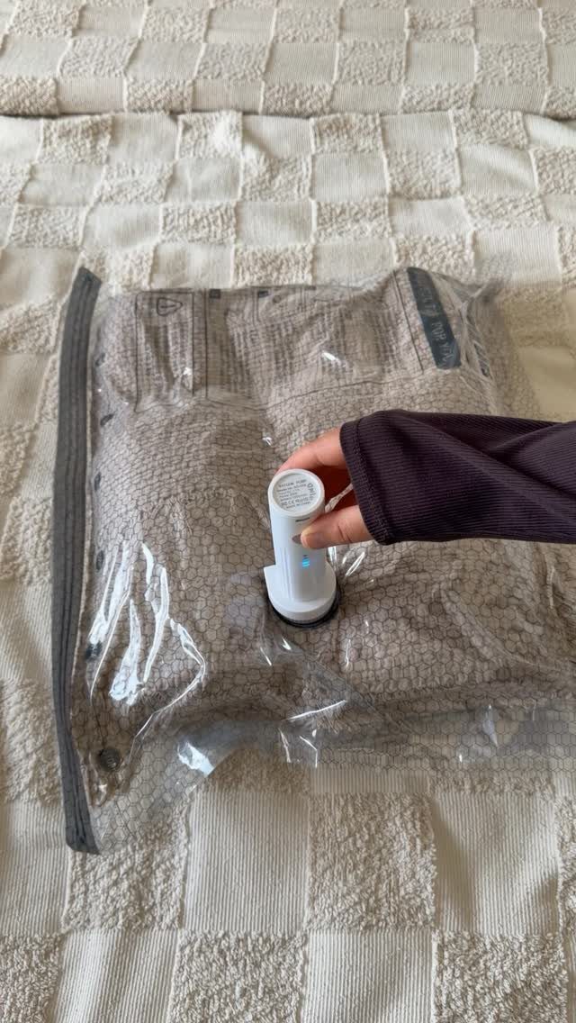 A hand using a vacuum pump to compress clothes inside a clear plastic storage bag.