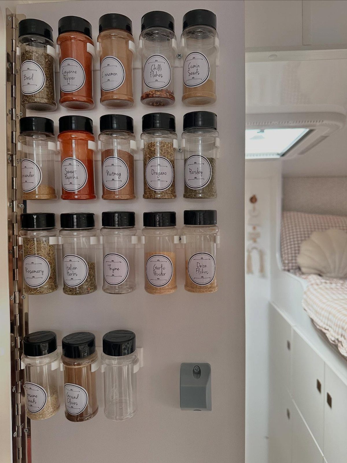 Clear spice jars with black lids mounted on a white wall inside a camper van.