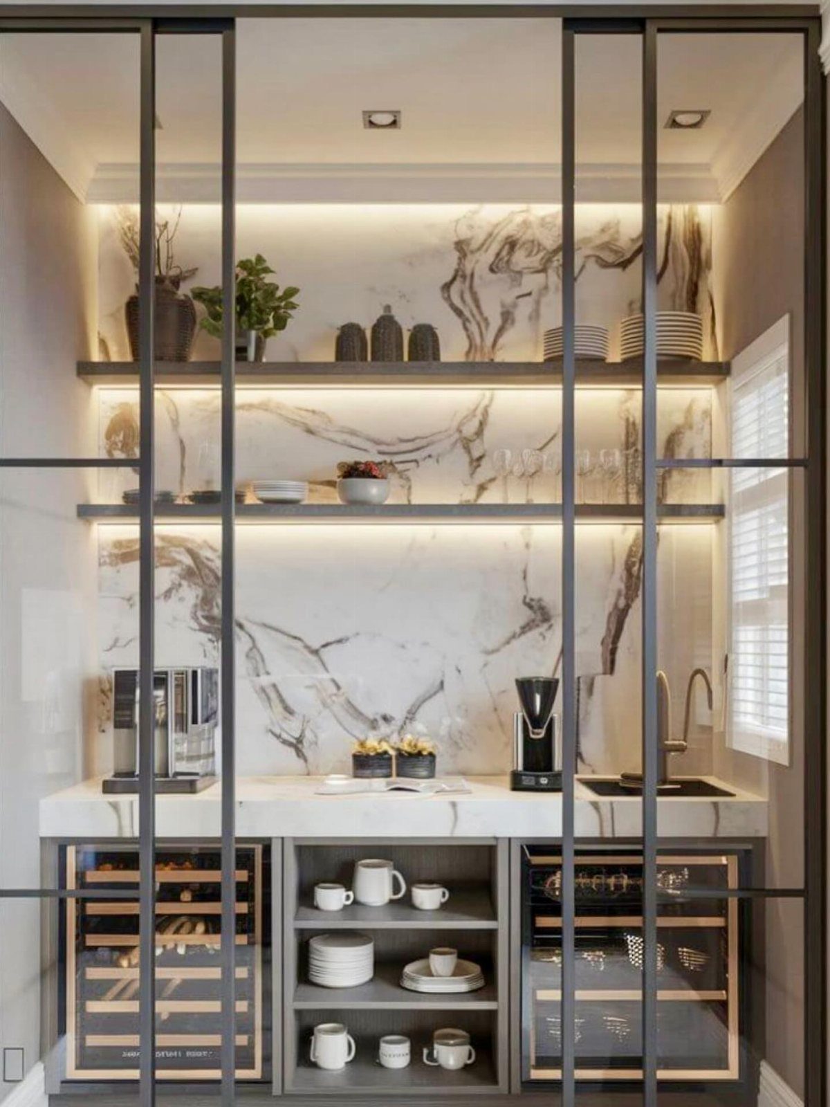 A luxurious built-in butler's pantry coffee bar with marble walls and illuminated shelving.