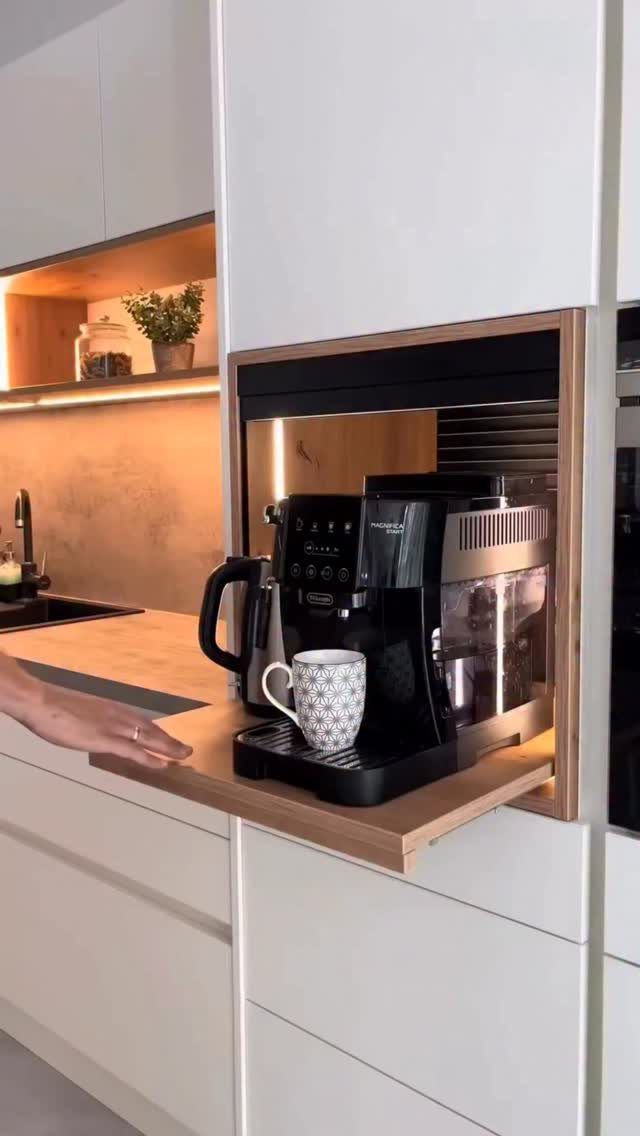 A black espresso machine on a wooden pull-out shelf within a white kitchen cabinet.