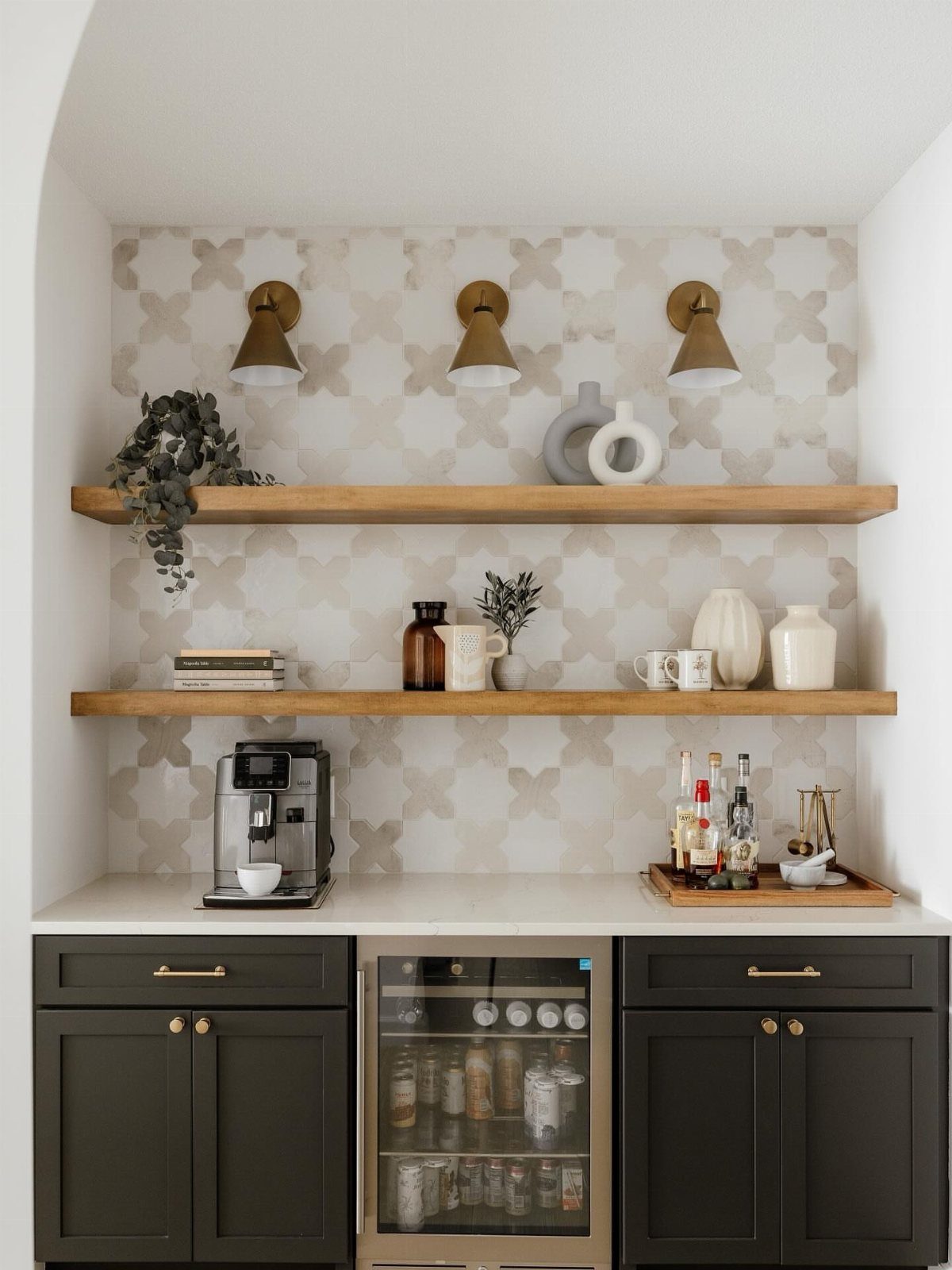 A coffee station with patterned tile backsplash, wooden shelves, and dark cabinets with a beverage fridge.
