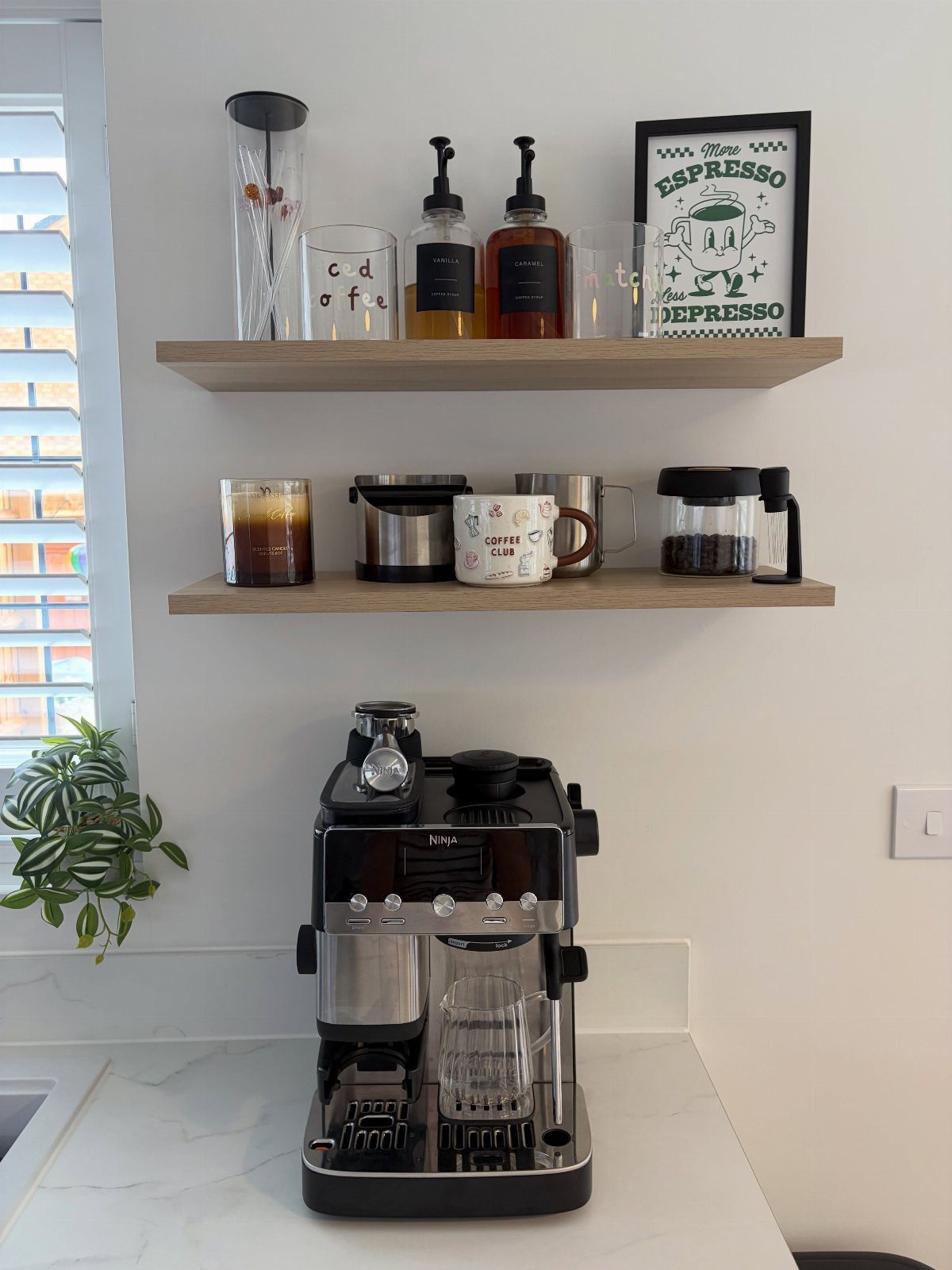 Black espresso machine on a marble counter with wooden floating shelves holding coffee accessories.