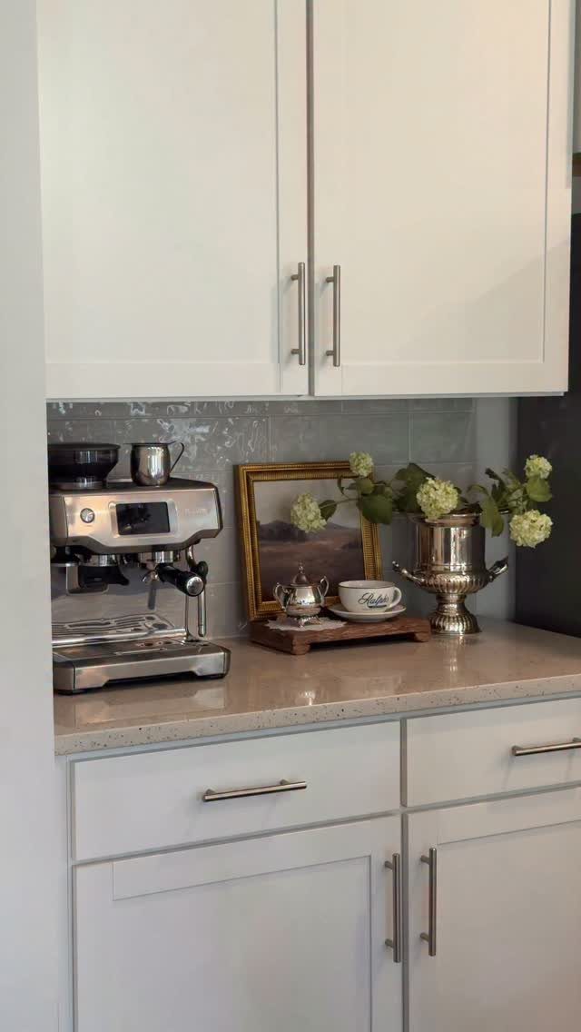 Silver espresso machine and vintage decor items sit on a white kitchen countertop.