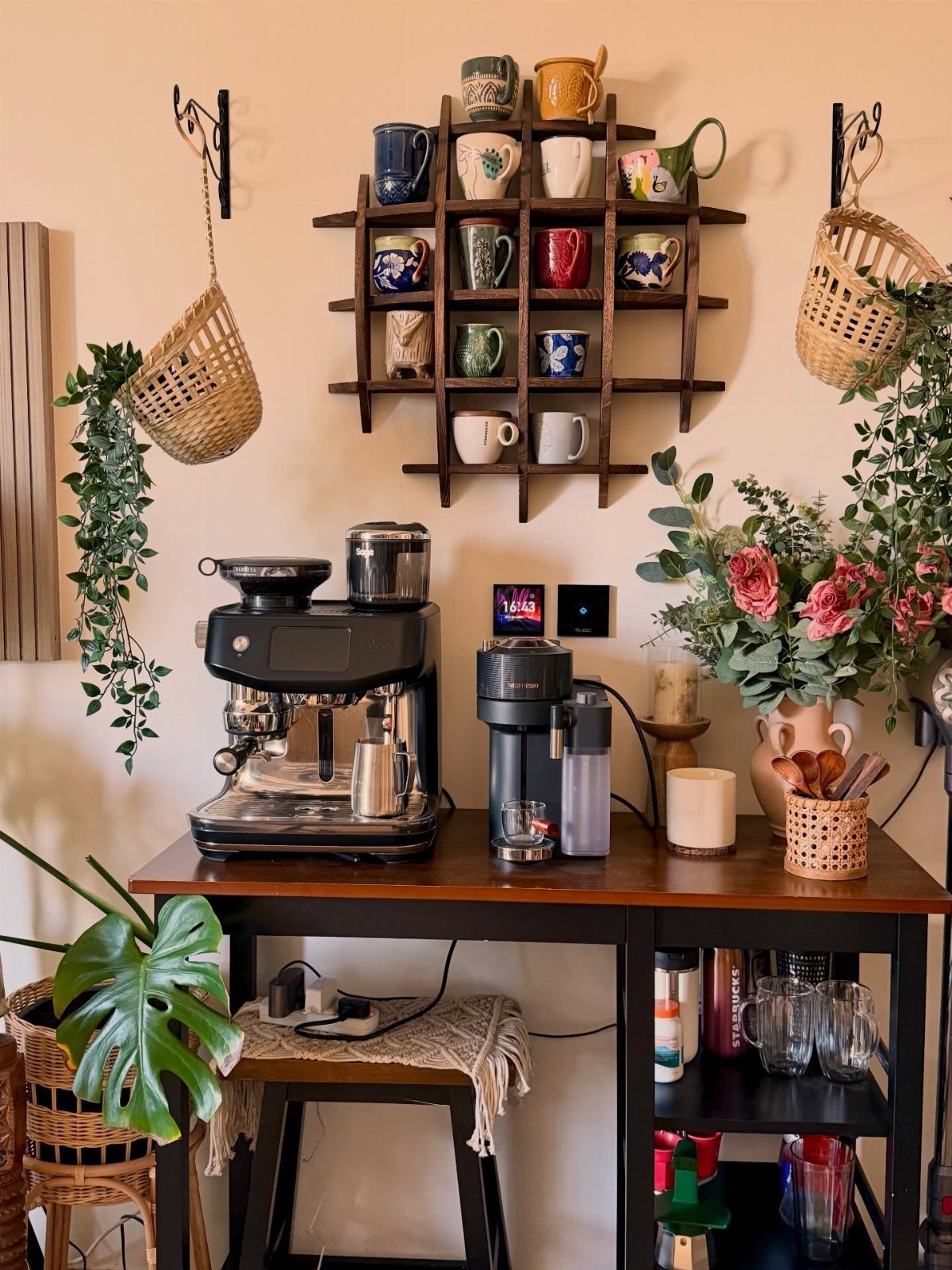 A wooden coffee station with an espresso machine, colorful mugs on a rack, and floral arrangements.