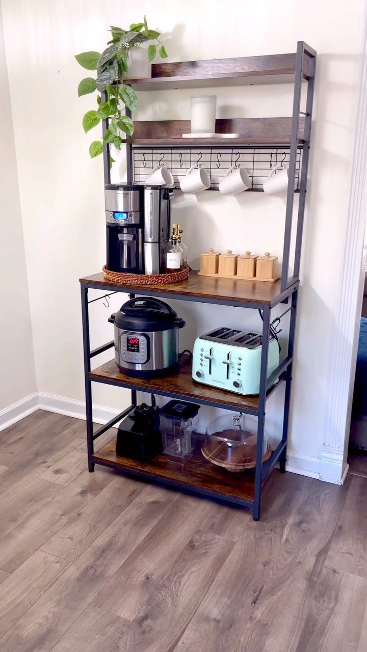 A dark wood and black metal shelving unit holding a coffee maker, toaster, and hanging mugs.