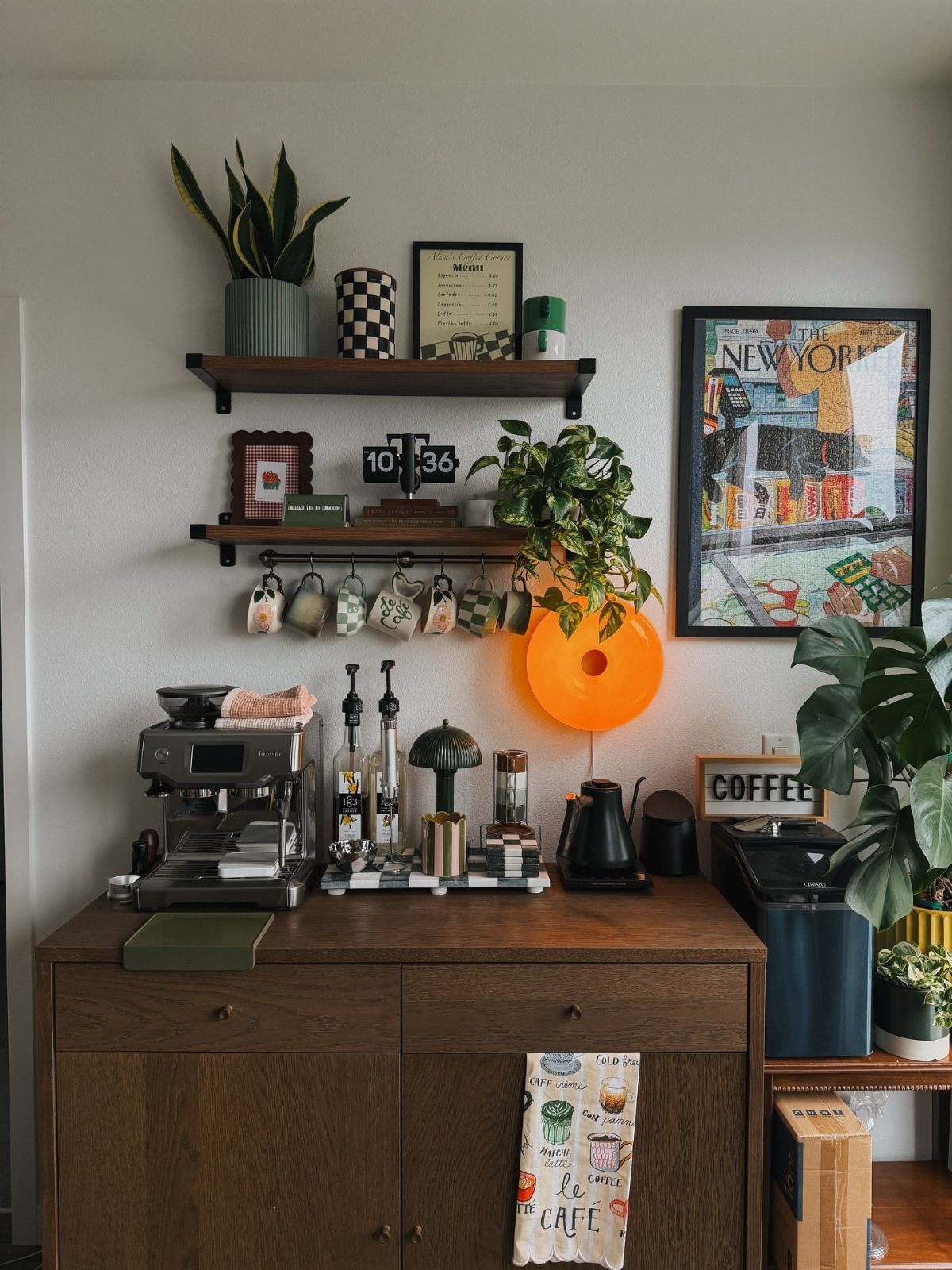 A wooden sideboard coffee station with an espresso machine, plants, and floating shelves on a white wall.