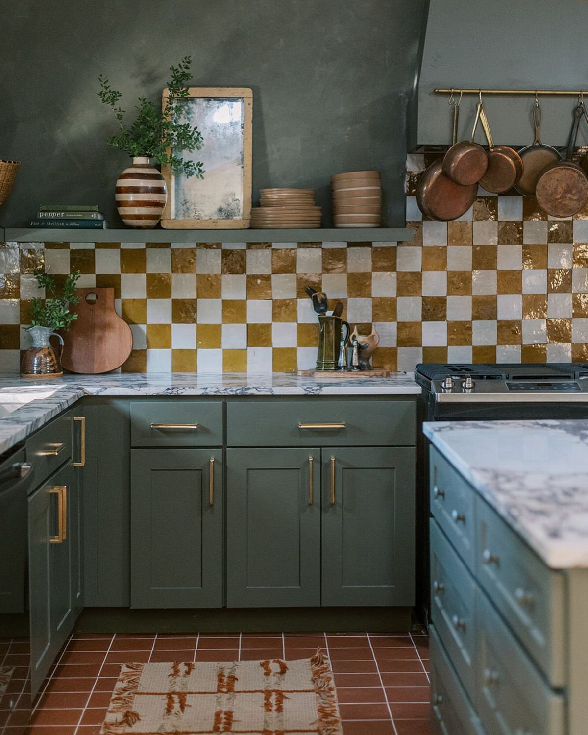 Green kitchen cabinets with a gold and white checkerboard tile backsplash and marble countertops.