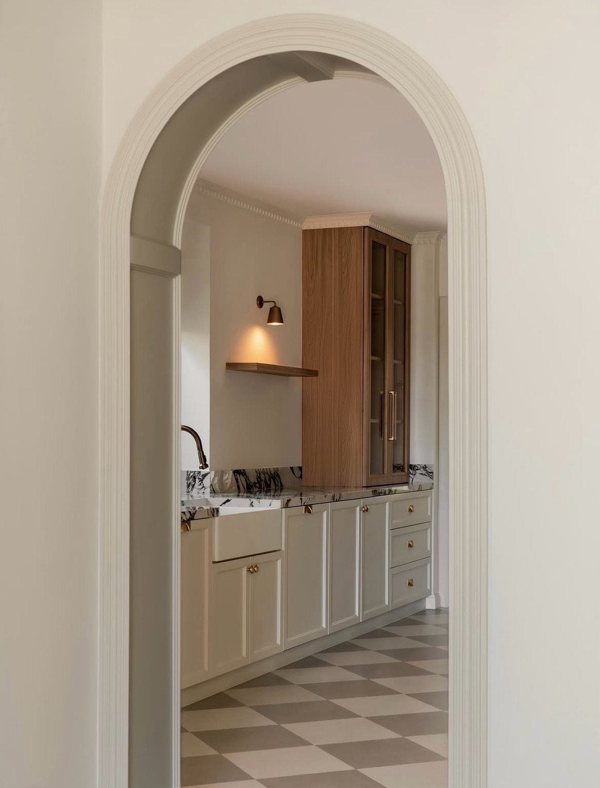 Checkerboard patterned floor visible through an arched doorway leading into a bright kitchen.