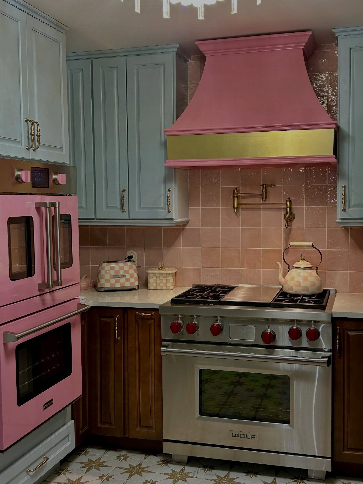 Pink range hood with gold trim above a stainless steel stove in a colorful kitchen.