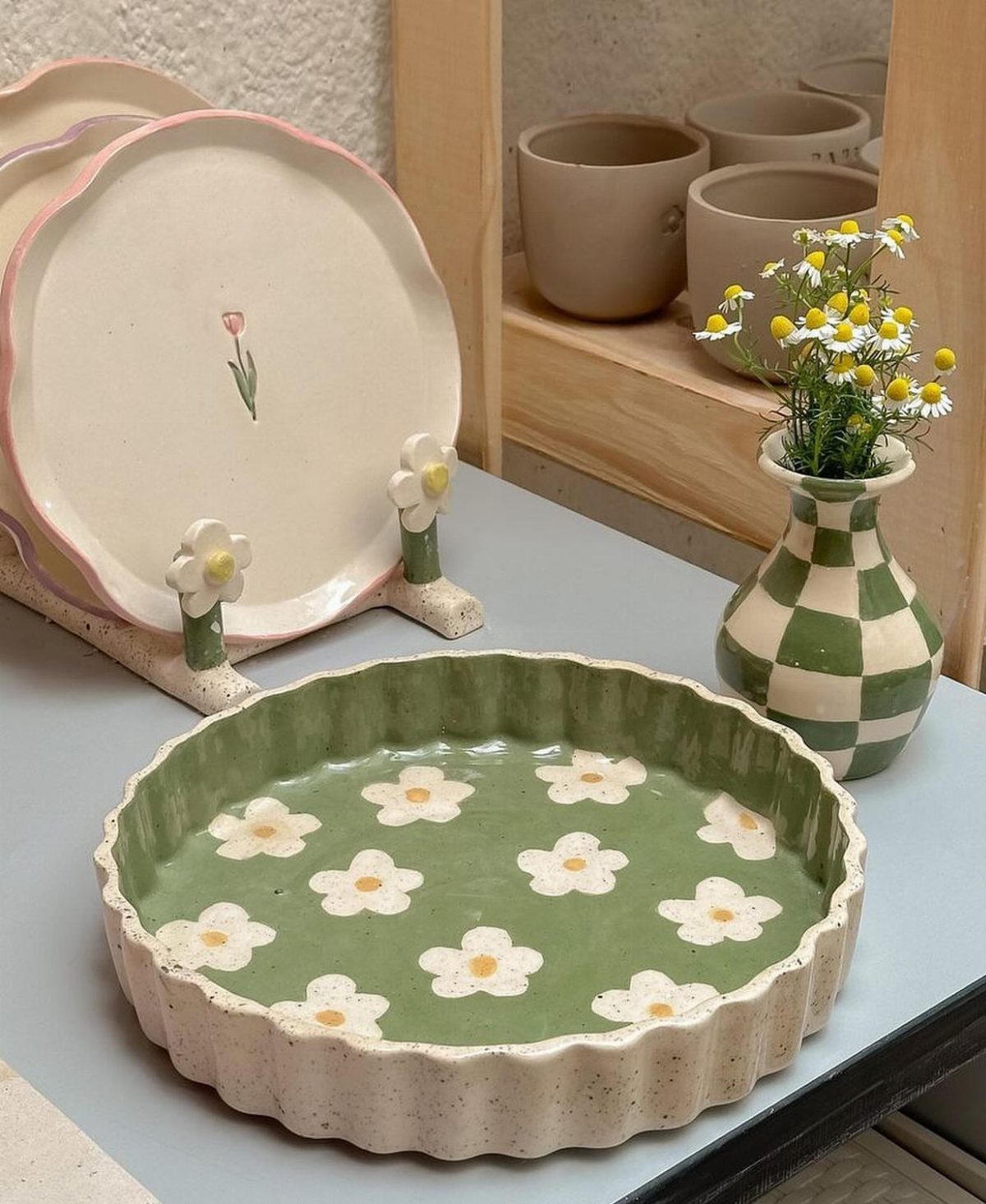 Decorative ceramic plates with floral patterns and a green daisy dish on a countertop.