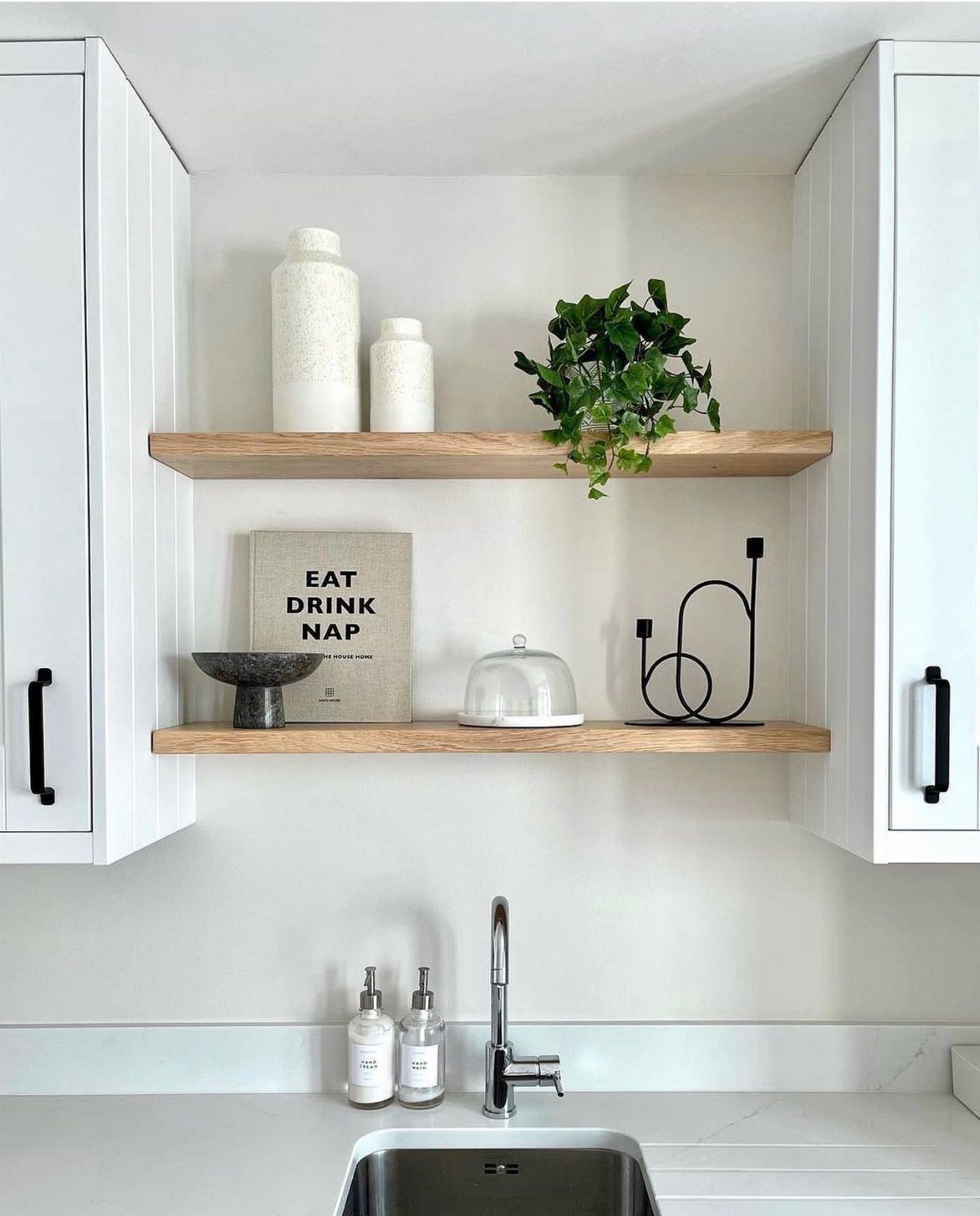 Two wooden floating shelves holding white ceramics and a small plant against a white wall.