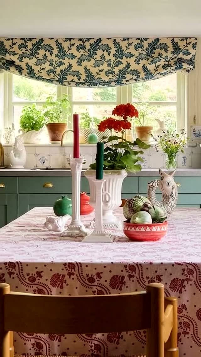 A patterned tablecloth on a dining table with candles and flowers in a kitchen.