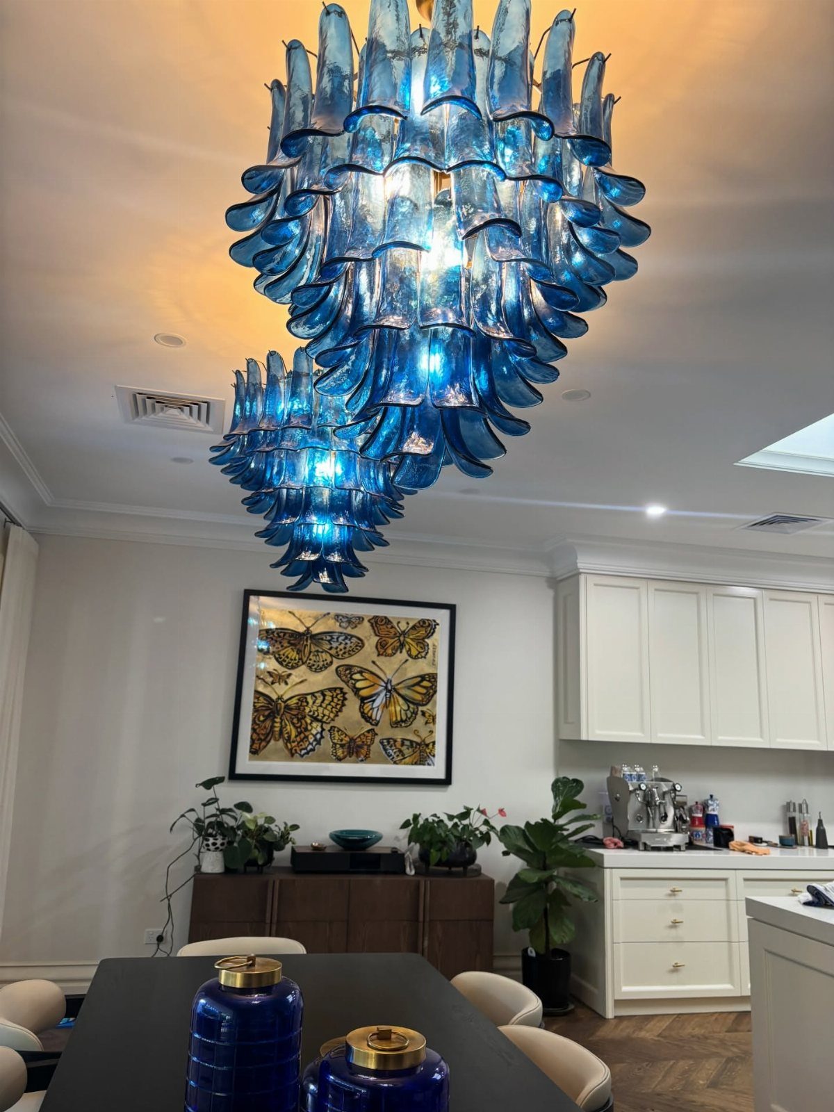 Two large, tiered blue glass chandeliers hanging in a modern dining room setting.